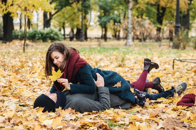 Felices mujeres y hombres disfrutan pasar tiempo juntos, yacen en el suelo cubierto de hojas amarillas