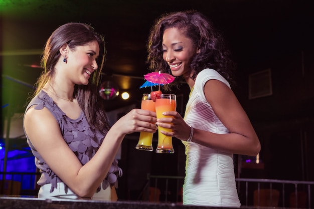 Felices mujeres jóvenes con cóctel en el bar