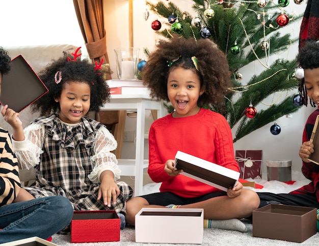 Felices los niños afroamericanos posan en una habitación con caja de regalo y adornos navideños