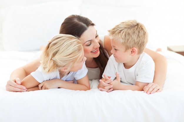 Felices niños y su madre hablando de acostarse en una cama