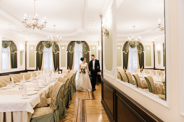 Felices novios jóvenes y amorosos van al salón de banquetes de un hotel de lujo. Día de la boda