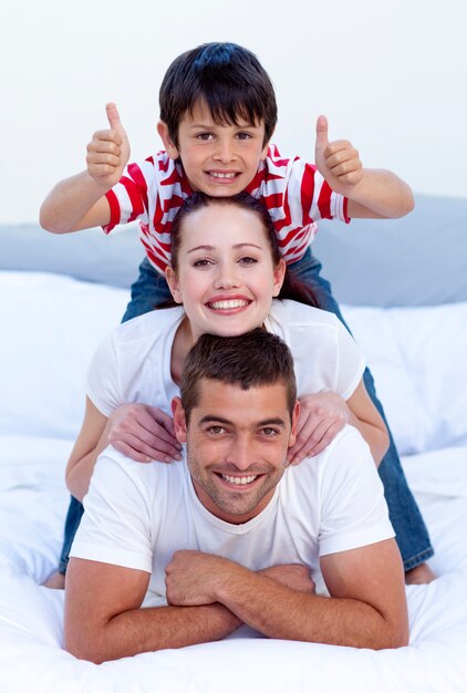 Felices padres e hijo en la cama con los pulgares arriba