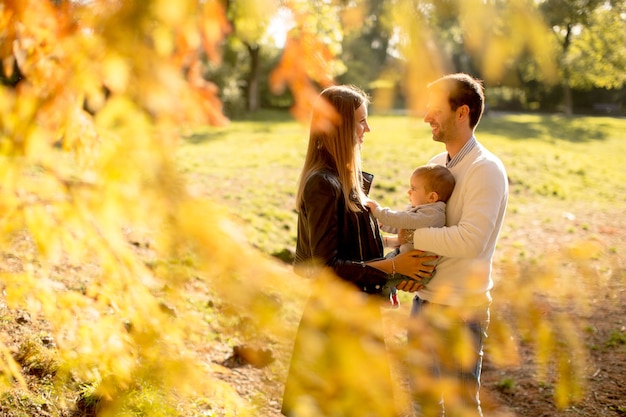 Felices padres jóvenes con bebé en el parque de otoño