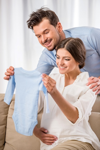 Felices padres jóvenes sostienen la ropa de su futuro bebé.