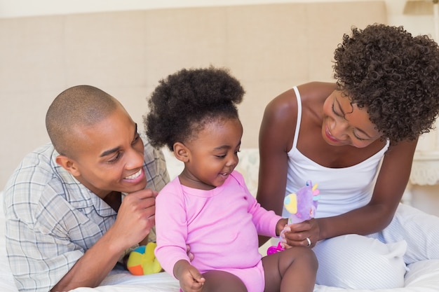 Felices padres jugando con la niña en la cama juntos