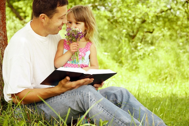 Felices padres con un niño leen la Biblia en el parque natural