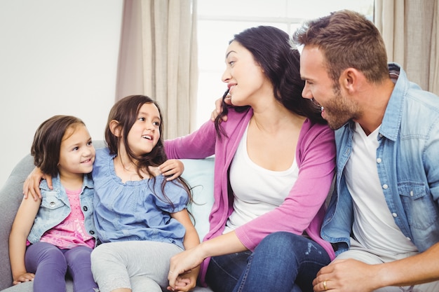 Felices padres sentados con hijas en el sofá