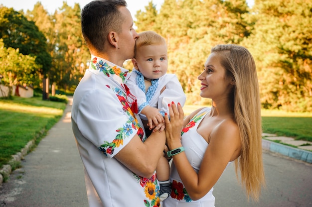 Felices padres sosteniendo en las manos un bebé vestido con la camisa bordada