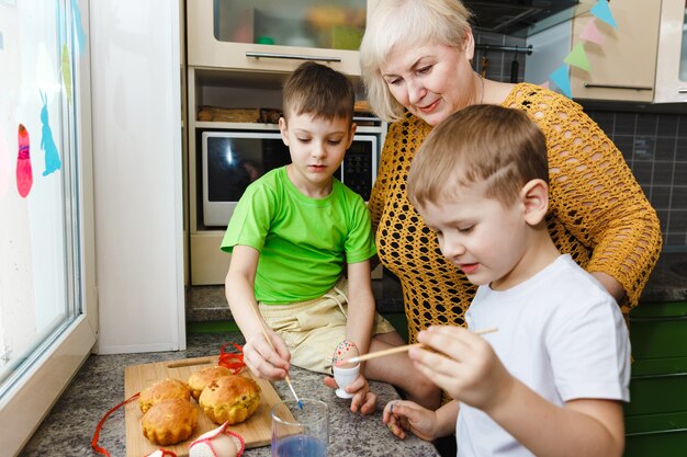 Felices Pascuas. Una abuela y sus nietos pintando huevos de Pascua. Familia feliz preparándose para la Pascua en casa