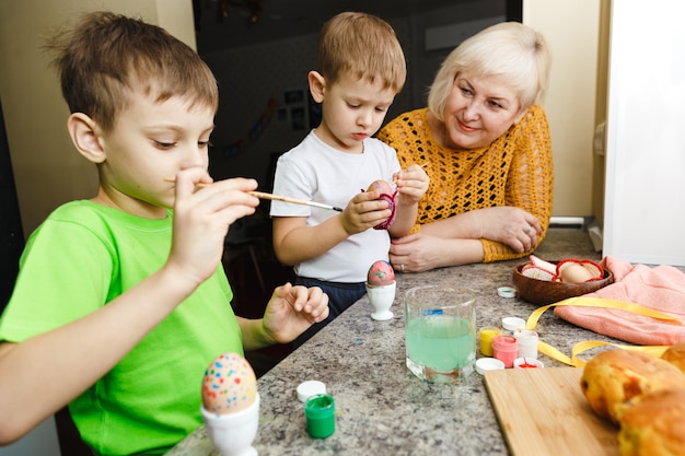 Felices Pascuas. Una abuela y sus nietos pintando huevos de Pascua. Familia feliz preparándose para la Pascua en casa