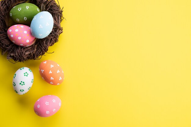 ¡Felices Pascuas! Colorido de huevos de pascua en nido con flor y pluma.