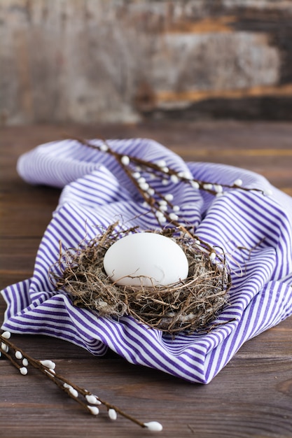 Felices Pascuas. Un huevo de gallina sin pintar en un nido de pájaro y ramas de sauce en una mesa de madera. .