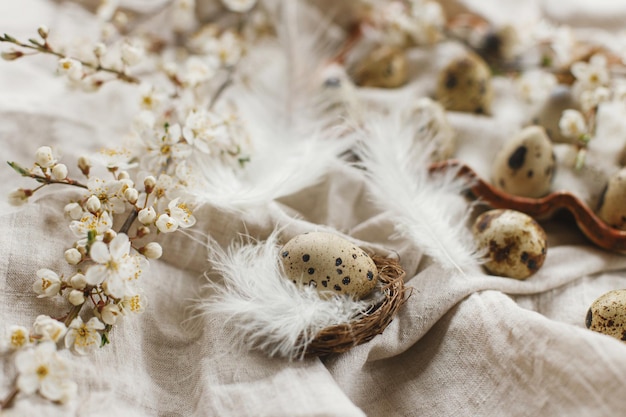 Felices Pascuas Huevos de Pascua con estilo y flores de primavera en flor en una mesa rústica Huevos de codorniz naturales en plumas de bandeja y tela de lino de flores de cerezo Bodegón de Pascua rústico