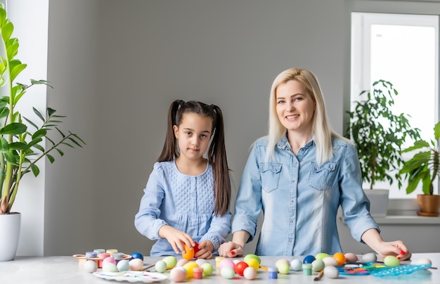 Felices Pascuas. Una madre y su hija pintan huevos de Pascua. Familia feliz preparándose para Pascua. Niña pequeña y linda con orejas de conejo el día de Pascua.