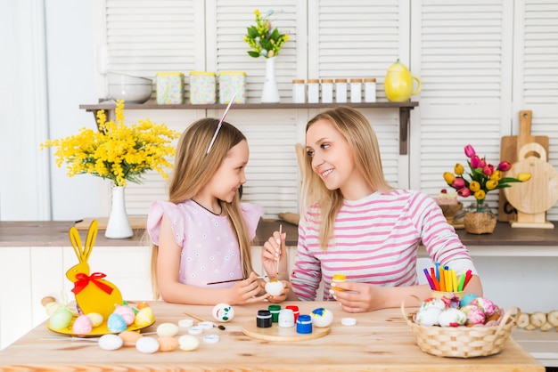 Felices Pascuas . Una madre y su hija pintan huevos de Pascua. Familia feliz preparándose para Pascua