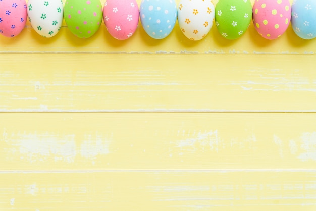 Foto ¡felices pascuas! reme los huevos de pascua en fondo de madera amarillo claro.