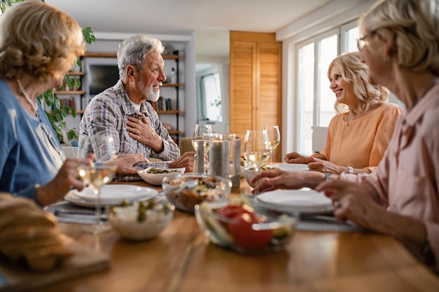 Felices personas mayores comunicándose mientras almuerzan juntos en la mesa del comedor