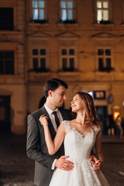 Felices recién casados se abrazan contra el fondo de la ciudad nocturna y las luces