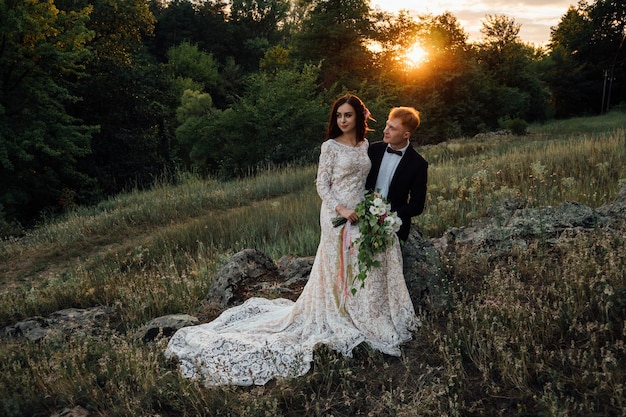 Felices recién casados están sentados en una roca en la naturaleza, puesta de sol