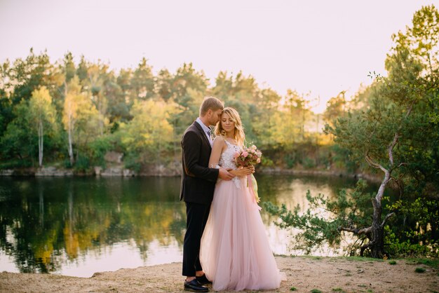 Felices recién casados de pie al atardecer