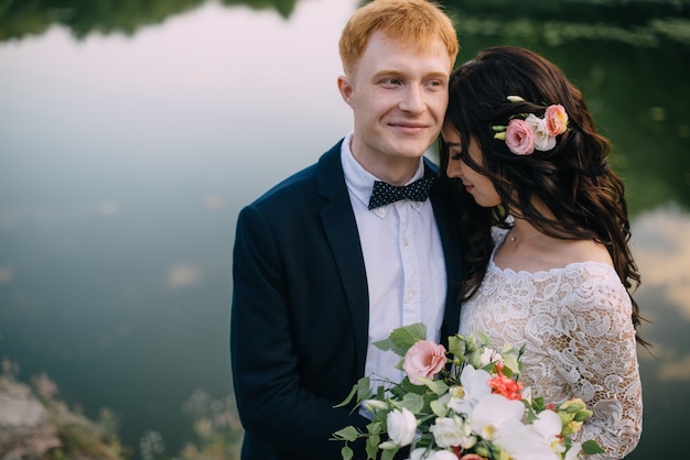 Felices recién casados de pie en la orilla del río