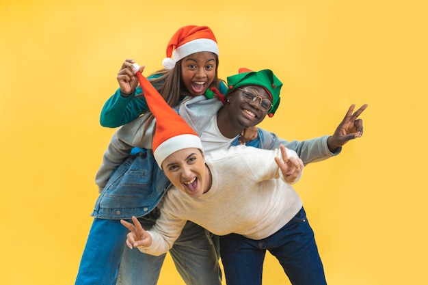 Felices tres amigos multirraciales celebrando la Navidad emocionada con fondo de estudio amarillo