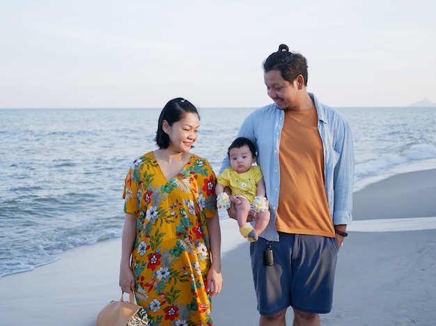 Foto felices vacaciones familiares asiáticas, mamá y papá sostienen a un lindo bebé en la playa, miran al bebé