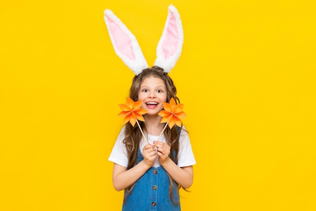 Felices vacaciones de Pascua Una hermosa niña con orejas de conejo en la cabeza celebrando un día de primavera Un niño en un vestido de verano sostiene flores de origami sobre un fondo amarillo aislado