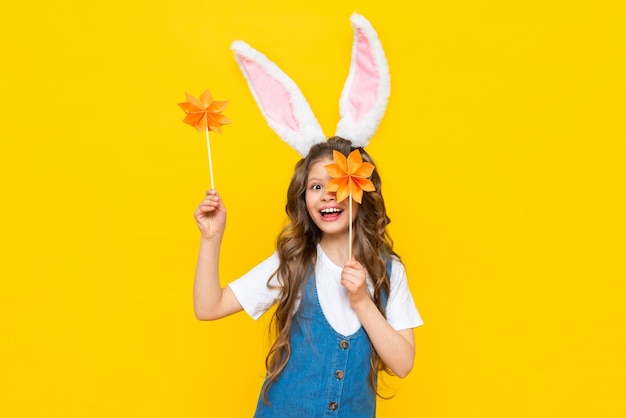 Felices vacaciones de Pascua Una hermosa niña con orejas de conejo en la cabeza celebrando un día de primavera Un niño en un vestido de verano sostiene flores de origami sobre un fondo amarillo aislado