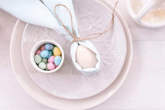 Felices vacaciones de pascua en la temporada de primavera decoración festiva del hogar comida tradicional huevo de gallina beige blanco envuelto en tela azul pálido como orejas de conejo o conejo en plato y pequeños huevos de caramelo en la mesa