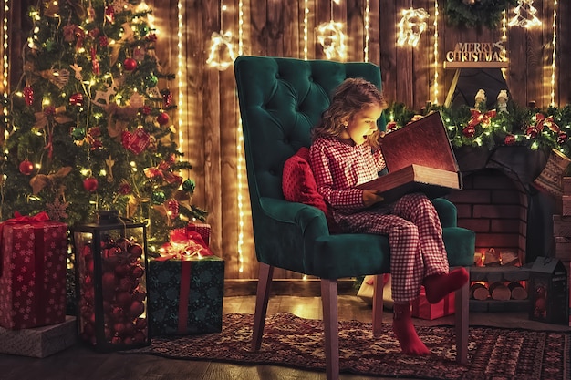 Felices vacaciones. Pequeño niño lindo que abre el presente cerca del árbol de navidad. La niña riendo y disfrutando el regalo.