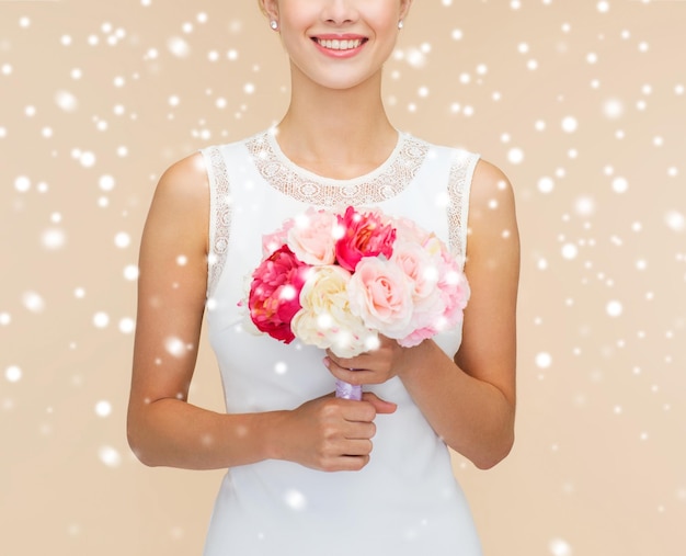 Felicidad, boda, vacaciones y concepto de celebración: cierre de novia sonriente o dama de honor vestida de blanco con ramo de flores sobre fondo beige y nieve