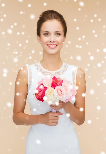 Felicidad, boda, vacaciones, gente y concepto de celebración - mujer sonriente vestida de blanco con un ramo de flores sobre fondo beige y nieve