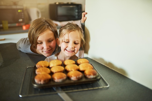 Felicidad casera Captura recortada de dos hermanos jóvenes mirando unos cupcakes recién horneados