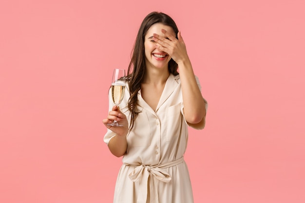 La felicidad, la celebración y el concepto de fiesta. Despreocupada, romántica y encantada mujer caucásica con un vestido lujoso, una carita sonriente mientras escucha una broma hilarante, diviértete, levantando copas de champán