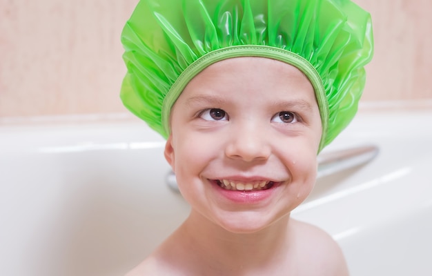 Felicidad de chico lindo con una gorra verde bañándose en la bañera