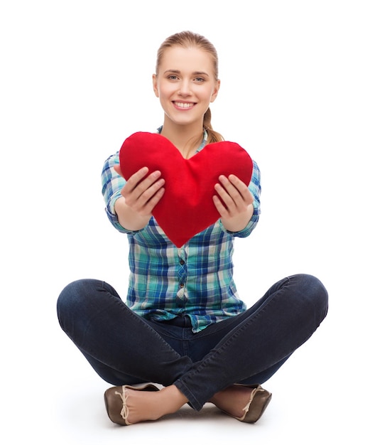 felicidad y concepto de la gente - mujer joven sonriente con ropa informal sentada en el suelo y sosteniendo el corazón rojo