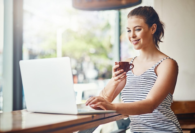 La felicidad es café recién hecho y wifi rápido Foto de una mujer joven usando su computadora portátil en una cafetería