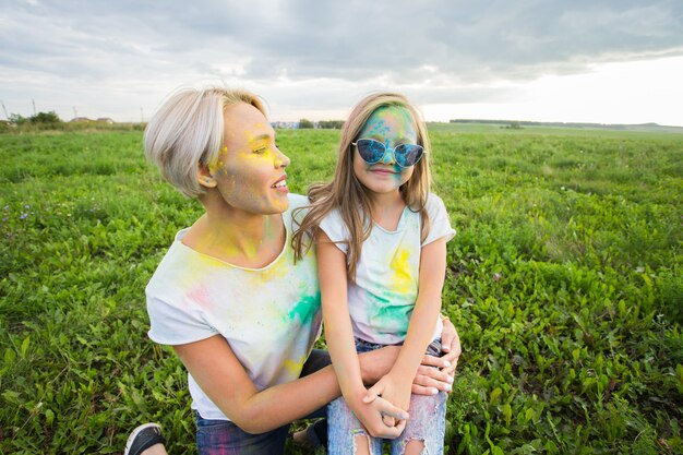 Felicidad, festival de Holi y concepto de vacaciones: madre e hija cubiertas con polvo de color