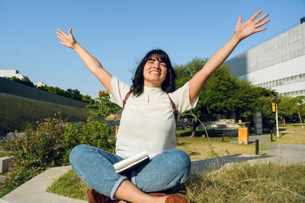 Felicidad y gratitud hacia la vida estudiante mujer latina sentada con los brazos abiertos y los ojos cerrados