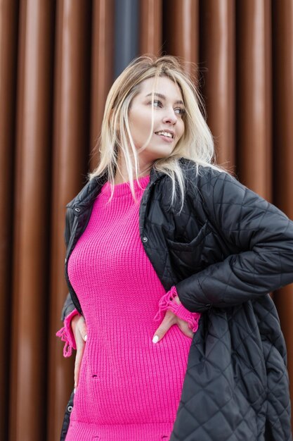 Felicidad hermosa mujer rubia con suéter rosa de moda y chaqueta camina por la calle