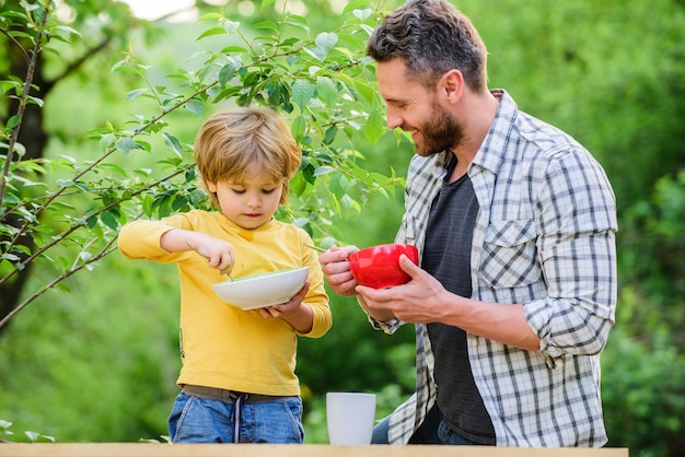 Foto felicidad de la infancia. comida para bebé. feliz día del padre. niño con papá desayunar. comida sana y dieta. productos lácteos. hijo y padre comiendo papilla de leche. familia feliz. cocinar sano.