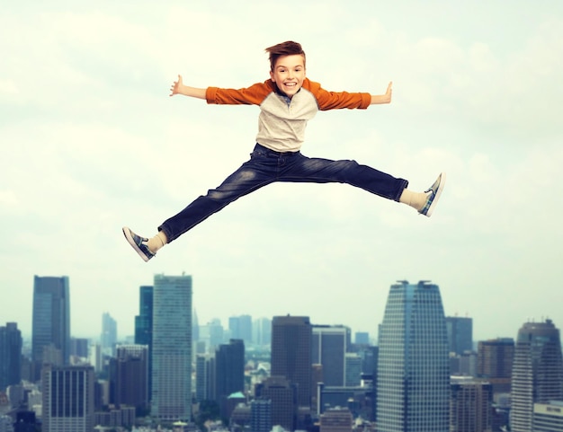 Foto felicidad, infancia, libertad, movimiento y concepto de la gente - niño sonriente feliz saltando en el aire sobre el fondo de la ciudad