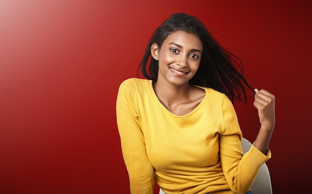 La felicidad irradia Retrato de estudio de una hermosa joven sentada en una silla contra un fondo rojo