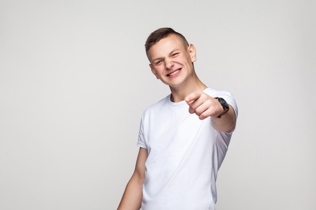 Felicidad joven apuntando con el dedo a la cámara y sonriendo con dientes. Tiro del estudio