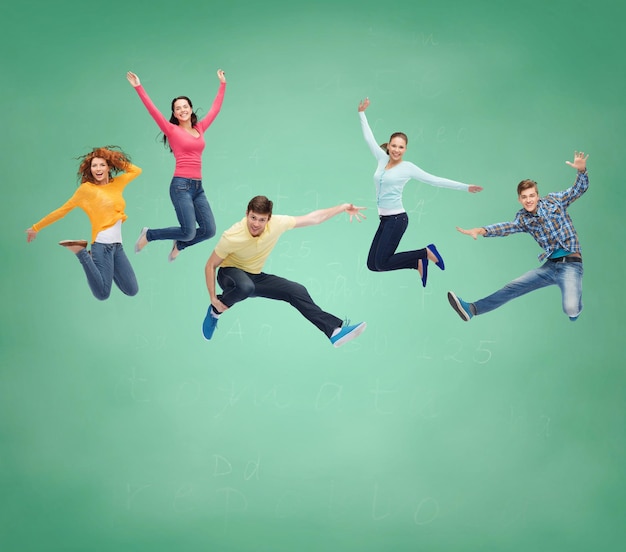 felicidad, libertad, amistad, educación y concepto de la gente - grupo de adolescentes sonrientes saltando en el aire sobre fondo de tablero verde