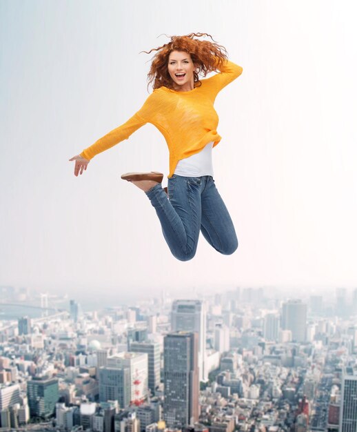 felicidad, libertad, movimiento y concepto de la gente - mujer joven sonriente saltando en el aire sobre el fondo de la ciudad