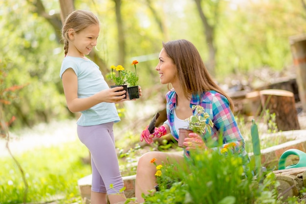 Felicidad linda niña ayudando a su madre sonriente a plantar flores en un patio trasero.
