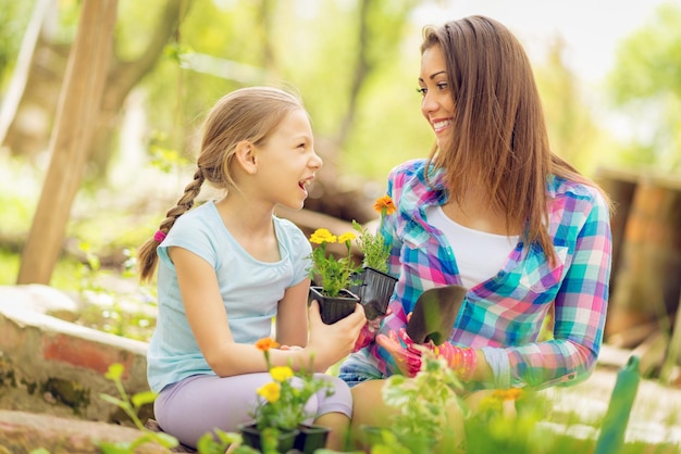 Felicidad linda niña y joven sonriente plantando flores en un patio trasero.