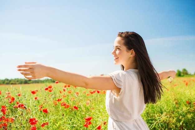 felicidad, naturaleza, verano, vacaciones y concepto de la gente - mujer joven sonriente en el campo de amapolas